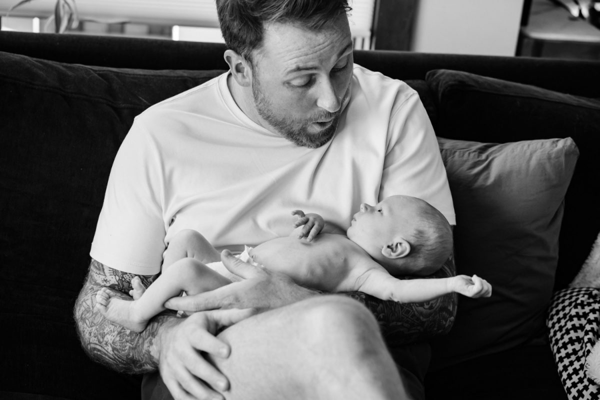 A newborn baby wiggles in his dad's arms during an at-home portrait session in Langford BC. 