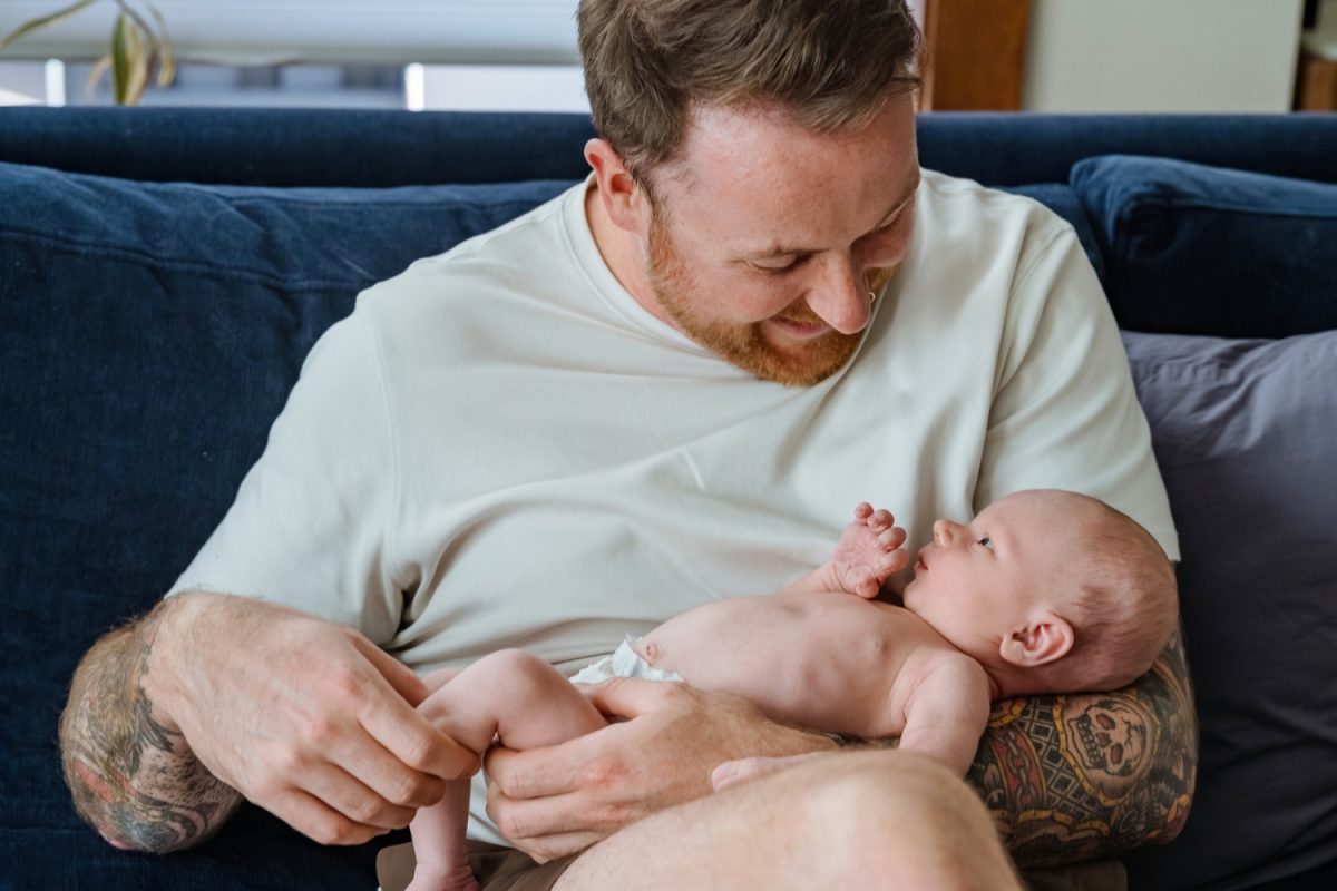 A colour photograph of a tattooed dad holding his baby boy during a newborn photo session in Victoria BC