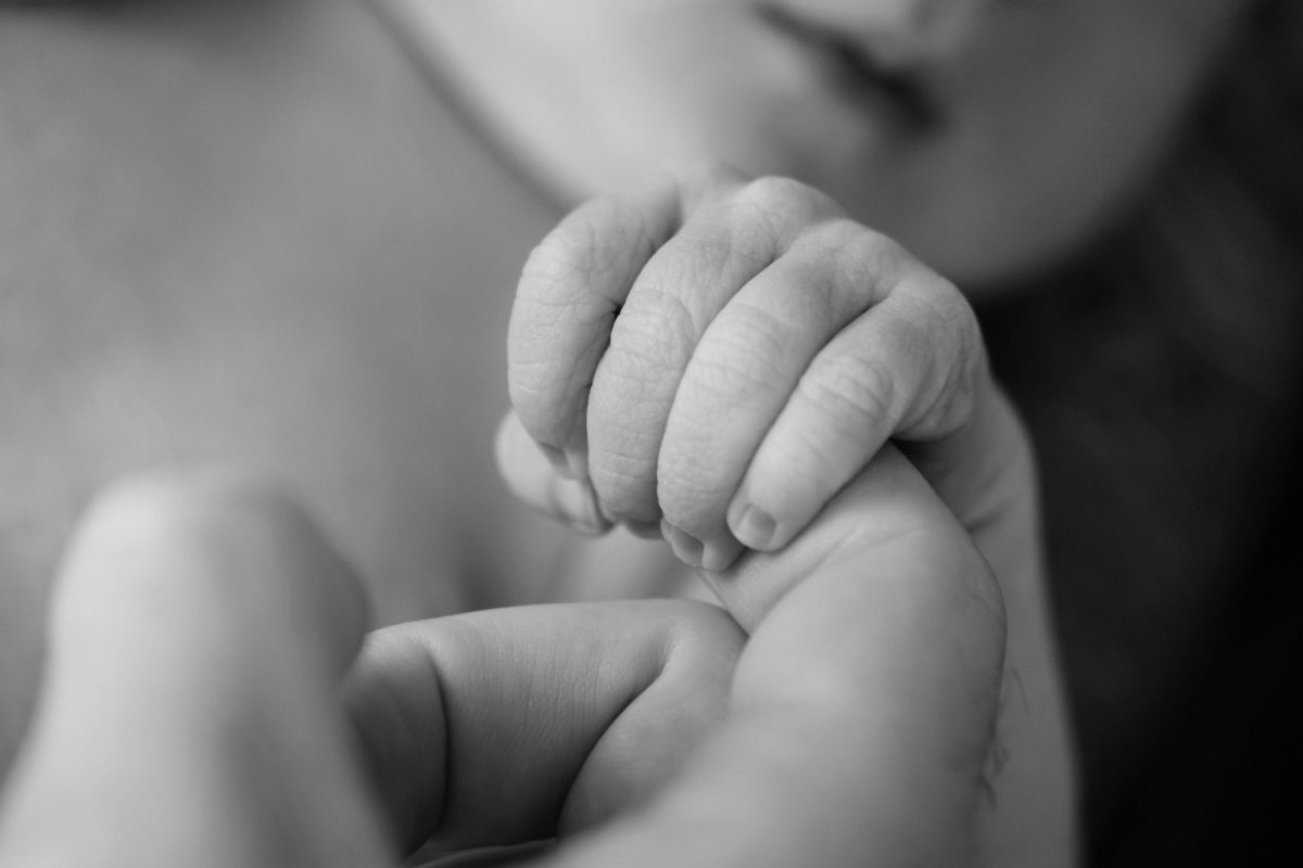 A closeup black and white detail of a baby's hand on his mom's finger. 