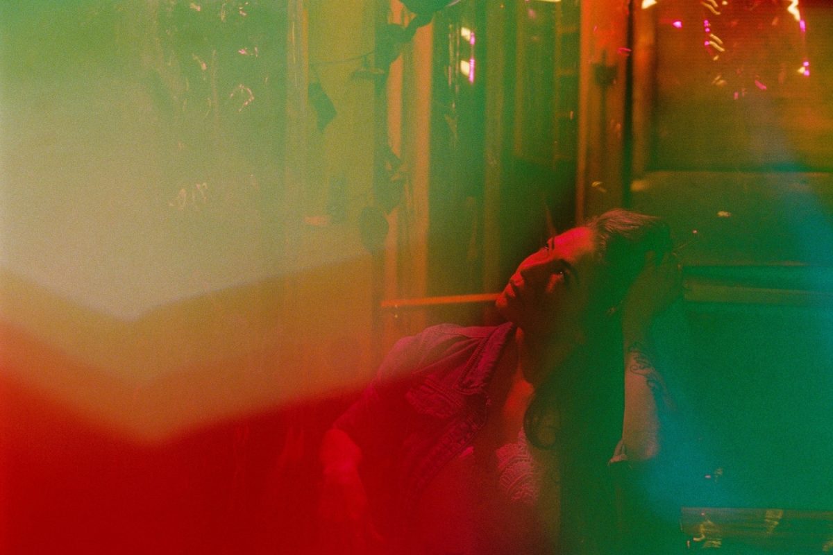 A cinematic mutli-coloured night photo of a woman in an empty restaurant. I used shiny dollar store objects to distort the foreground.