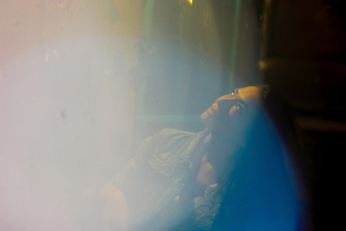 A cinematic mutli-coloured night photo of a woman in an empty restaurant. I used shiny dollar store objects to distort the foreground. Taken with Cinestill 800T medium format 120 film. The image has a dreamy and hazy quality.