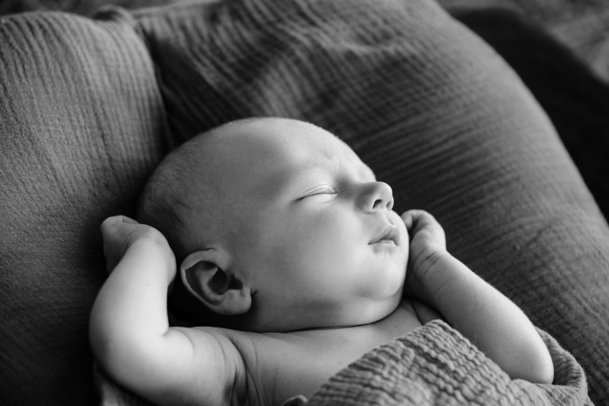 A black and white candid photo of a sleeping newborn baby during a newborn portrait session in Langford BC