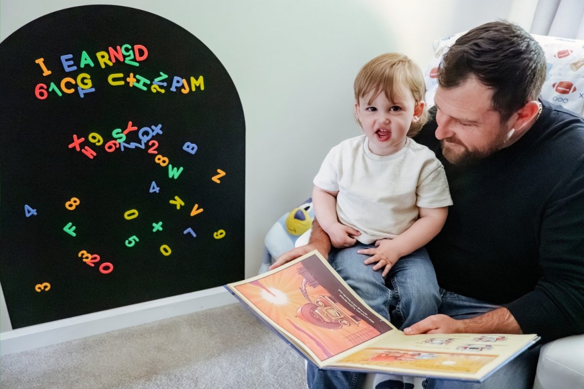 A toddler sits on his father's knee and reads a story during at-home candid family photos in Victoria BC