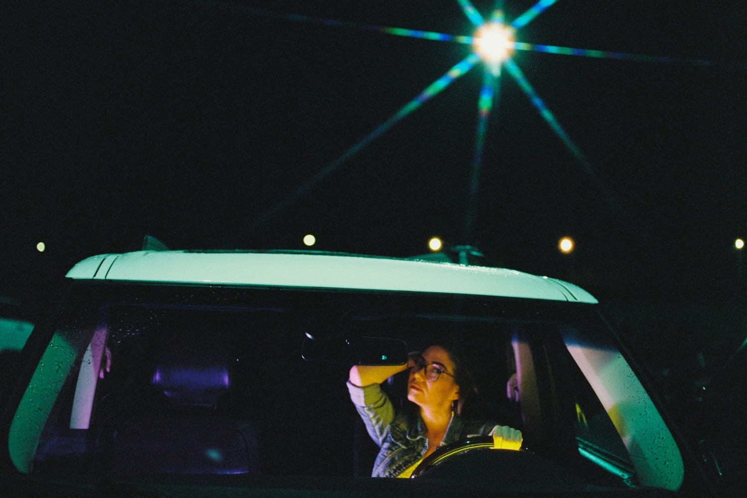 A cinematic portrait of a woman in a car illuminated by ambient and video lights using Cinestill 800T 120 medium format film. The image was taken in a parking lot at Fisherman's Wharf in Victoria BC and the street light looks like a star because of a filter I used on the lens.