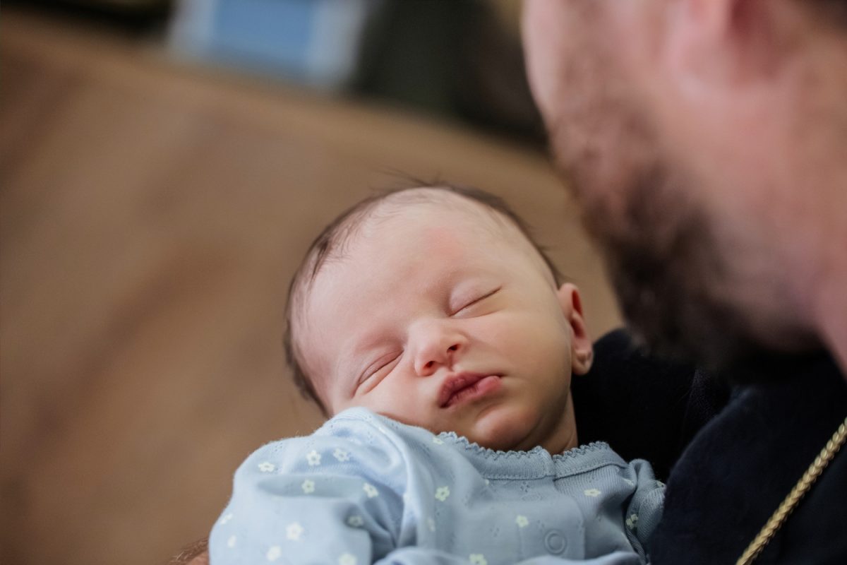 A newborn baby asleep in her father's arms during a newborn baby photo session at home in Victoria BC