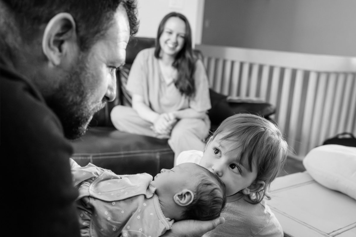 A toddler kisses his new baby sibling's forehead during a candid documentary photography session in Victoria BC in the family's home.