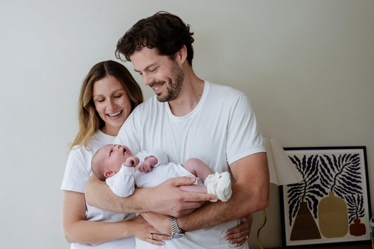 Victoria BC newborn photography at home in colour. The parents are holding their daughter and smiling while they look at her.