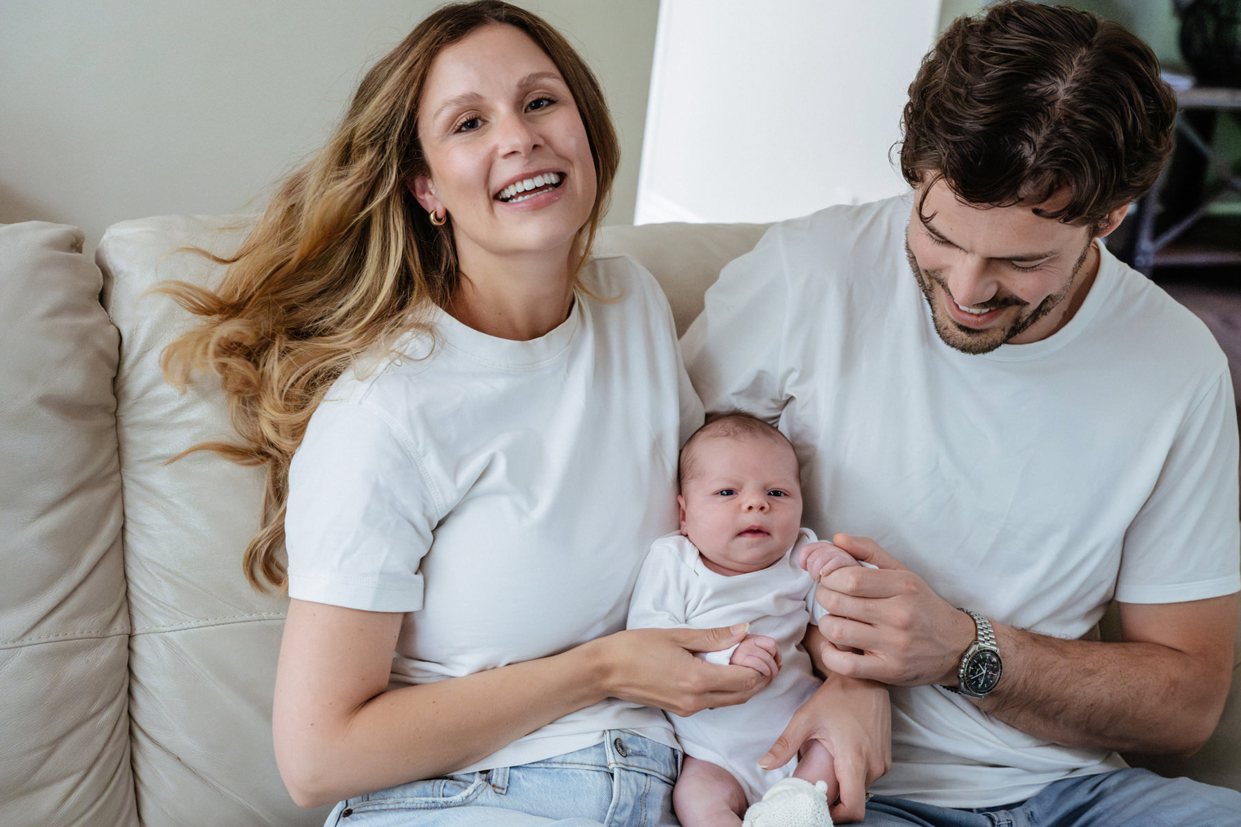 A couple holds their baby on their couch during their at home Victoria BC candid newborn mini session.
