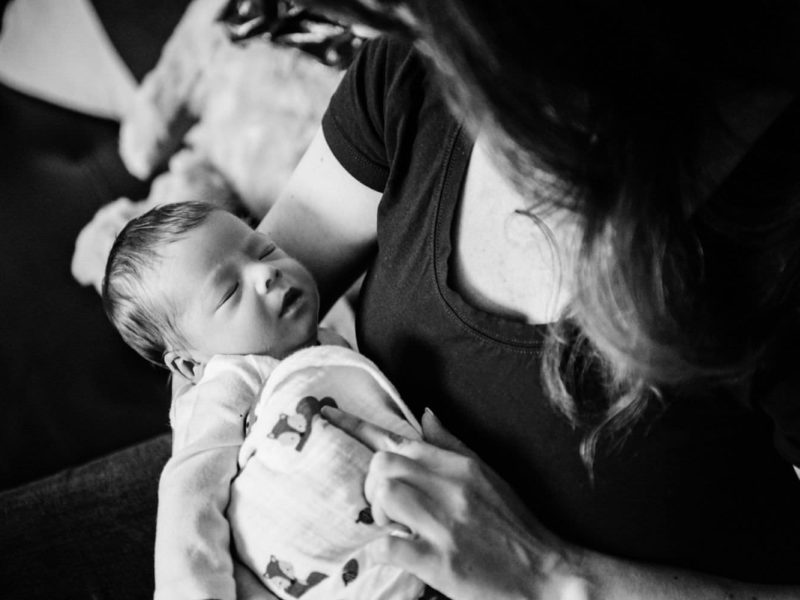 A mother holds her newborn baby. Photo is taken in black and white and it's a documentary family portrait.