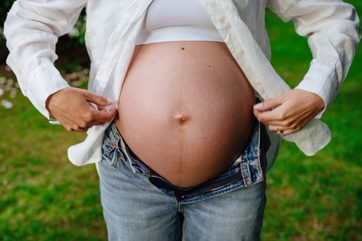 a maternity pregnancy photo of a mom-to-be in Victoria BC showing off her baby belly. She is wearing a white shirt and jeans and the photo is taken in the backyard of their home.