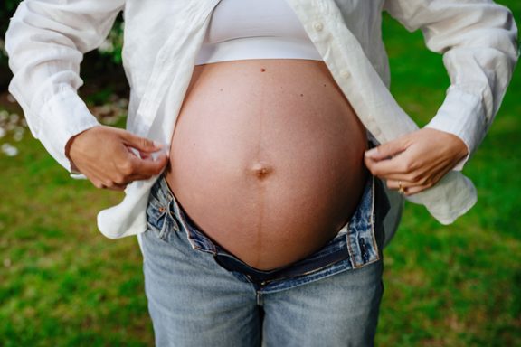 a maternity pregnancy photo of a mom-to-be in Victoria BC showing off her baby belly. She is wearing a white shirt and jeans and the photo is taken in the backyard of their home.