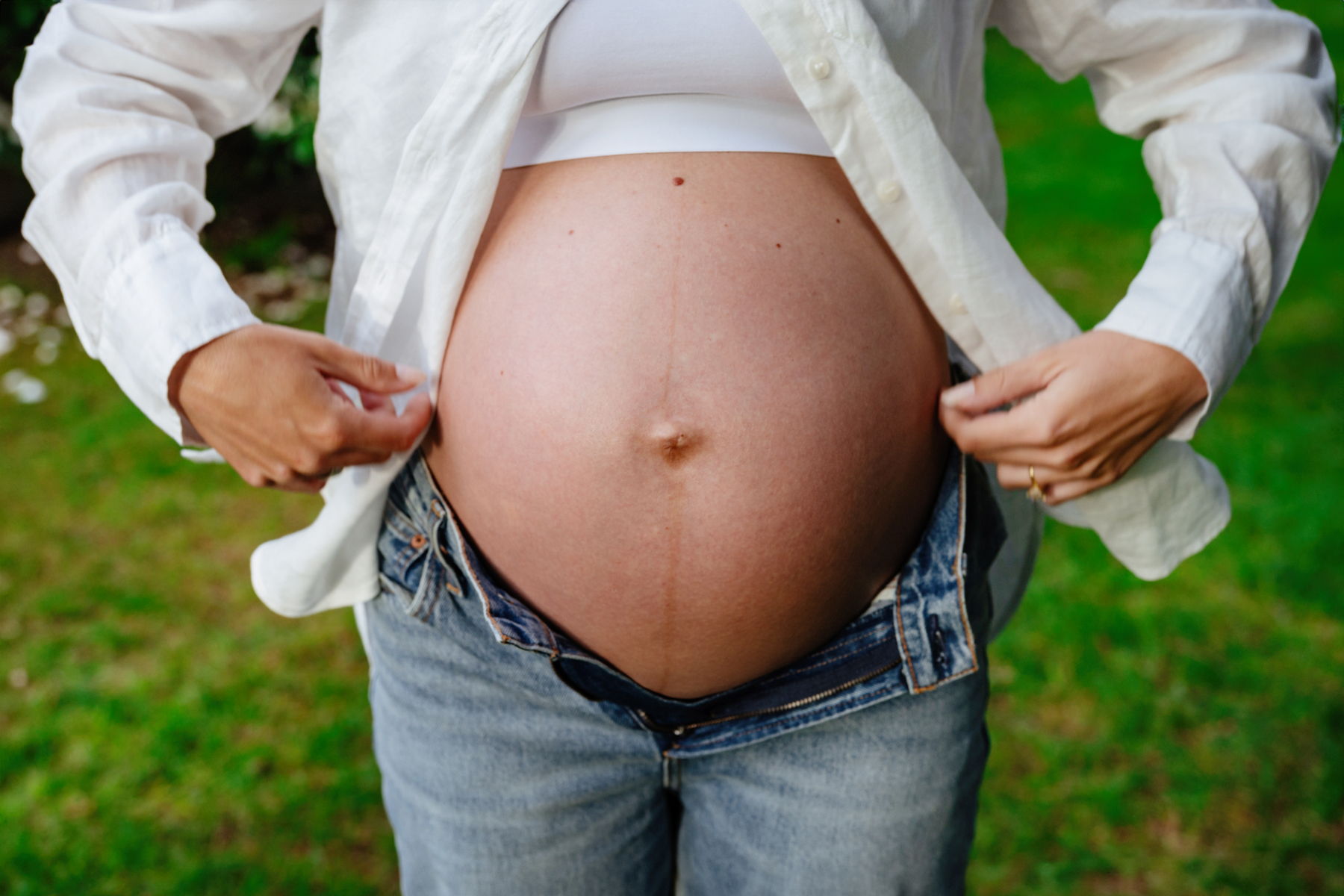 a maternity pregnancy photo of a mom-to-be in Victoria BC showing off her baby belly. She is wearing a white shirt and jeans and the photo is taken in the backyard of their home.