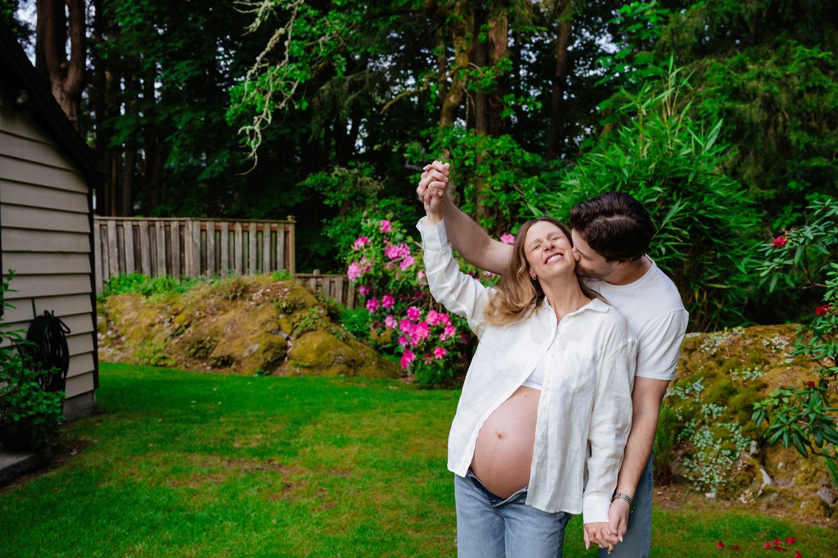 A playful candid maternity portrait of a couple expecting a baby in their backyard and garden in Victoria BC