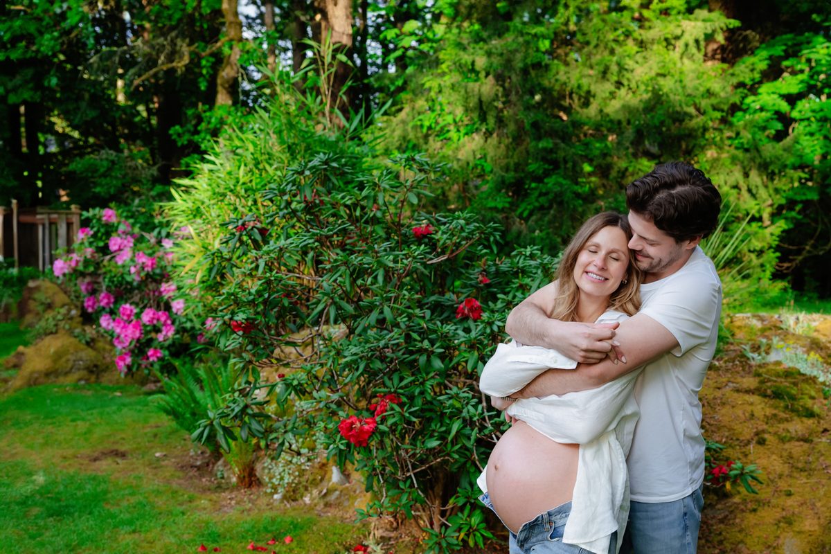 In Victoria BC a couple cuddles and shows off mom-to-be's baby belly during a pregnancy maternity portrait session in their backyard at their home.