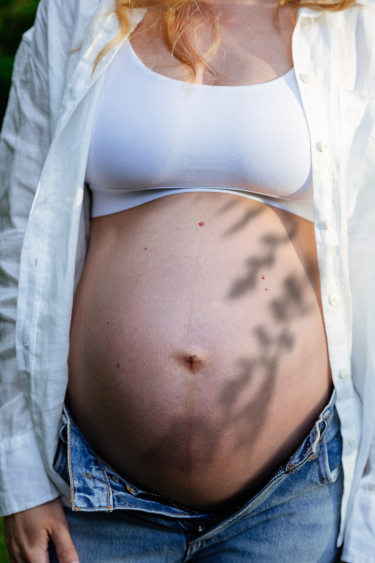 A shadow over the belly of a pregnant mother-to-be in the backyard of the family home in Victoria BC during a maternity session